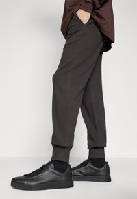 Dunkelgraue Jogginghose mit seitlichen Taschen und gerippten Bündchen, kombiniert mit schwarzen Sneakers mit glatter Oberfläche und minimalem Design.