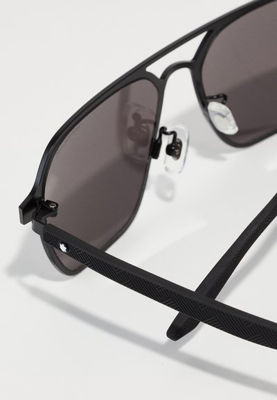 Ochelari de soare negri cu un design elegant, având lentile închise la culoare și brațe negre texturate cu un model geometric și tampoane nazale transparente.