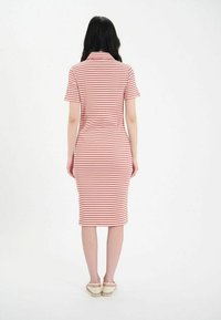 Robe à rayures rouges et blanches arrivant aux genoux, avec des manches courtes et une silhouette ajustée, fabriquée dans un matériau doux et extensible. Vue arrière simple.