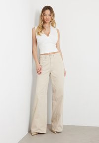 Pantalones de pierna ancha color beige con una cintura alta y una textura suave, combinados con una blusa ajustada sin mangas blanca, sobre un fondo neutro.
