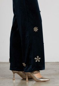 Pantalones de terciopelo azul marino con embellimientos florales metálicos y tacones dorados con diseño de tiras y punta afilada.