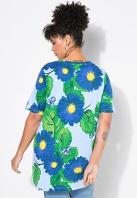 T-Shirt s modrým květinovým vzorem, se velkými modrými květy se žlutými středy a zelenými listy na světle modrém pozadí; krátké rukávy, uvolněný střih.