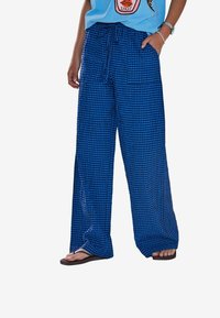 Pantalon large à carreaux bleus avec taille à cordon de serrage et poches latérales, fabriqué en tissu léger, offrant une coupe ample et un design décontracté.