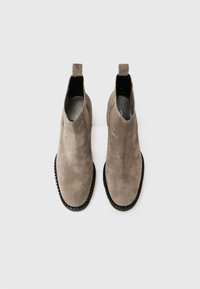 Bottines en daim gris avec un bout arrondi, semelle en caoutchouc noir contrastant et languettes pour un enfilage facile. Surface texturée avec des coutures visibles.