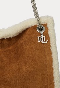 Barna velúr táska krém színű műsherling díszítéssel, ezüst lánc pánttal és kör alakú ezüst hardware elemmel, amelyen az "RL" logó található.