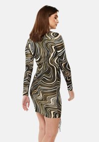 Long-sleeve dress in a wavy black, cream, and gold pattern. Tailored fit with side ruching and slits at the hem for added detailing.