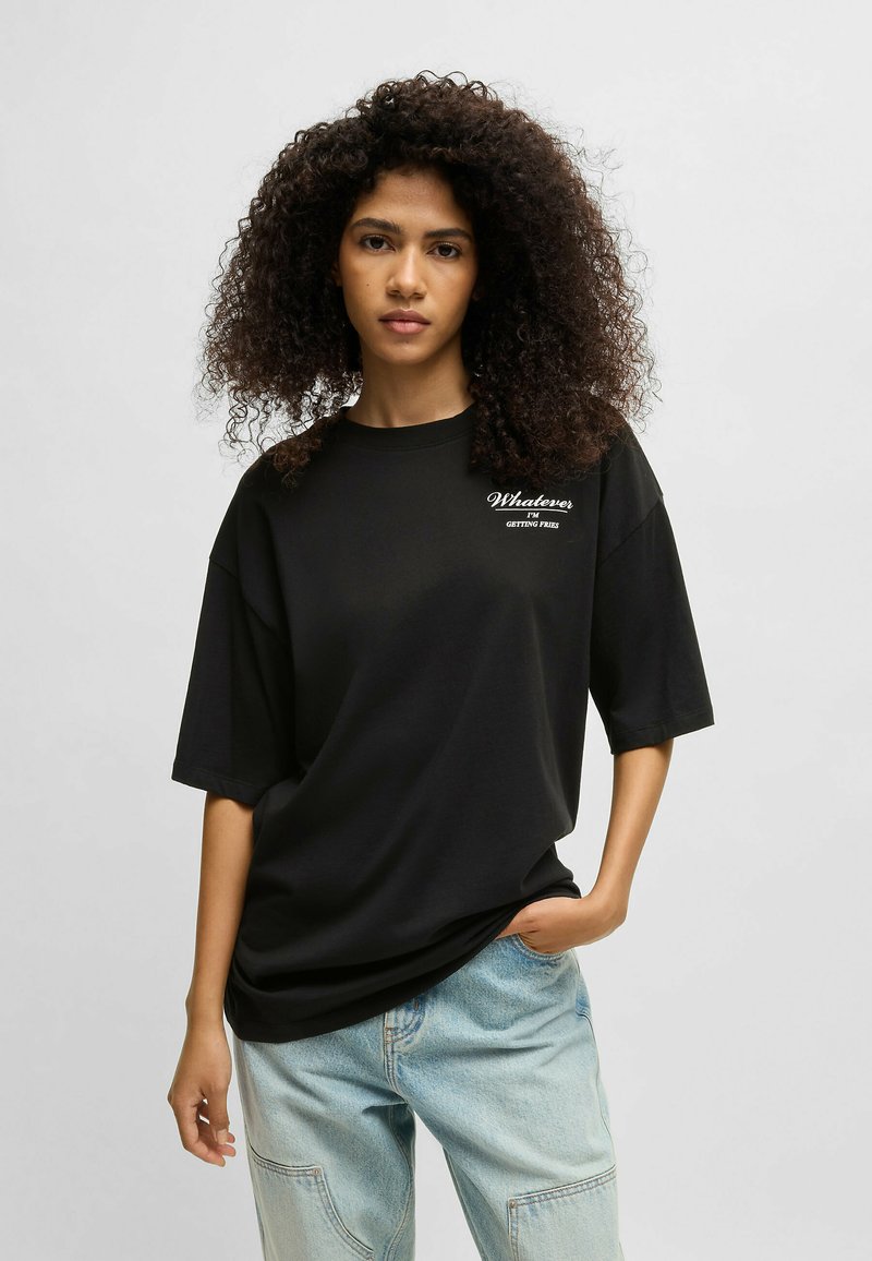 Black oversized t-shirt with short sleeves, featuring white text "Whatever I'm getting free" on the left chest area. Soft fabric texture.