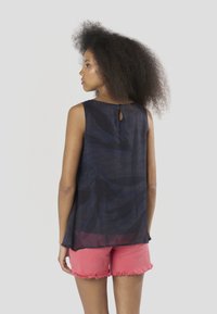 Tengerészkék ujjatlan blúz kulcslyuk részlettel a hátán, texturált mintával. Rózsaszín, rojtos farmer rövidnadrággal párosítva.