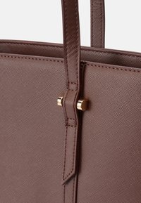 Smeđa torba bez rukava izrađena od teksturiranog materijala, s elegantnim ručkama i zlatnim detaljima. Simple dizajn s minimalnim šavovima.