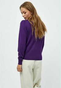 Lila Strickpullover mit langen Ärmeln, gerippten Bündchen und Saum. Glatte Textur, taillierte Passform, kombiniert mit cremefarbenen Hosen.