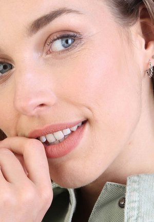 Close-up van een persoon met lichte huid, die zilveren oorringen en een lichtgroene stoffen kraag draagt. Heeft een egale huid en lichte make-up.