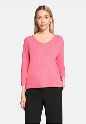 Pull en maille côtelée rose avec un décolleté en V et des manches trois-quarts, associé à un pantalon noir. Le matériau semble doux et texturé.