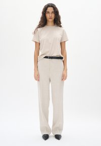 Beige t-shirt met korte mouwen en lichtgekleurde wijde linnen broek, vastgemaakt met een zwarte riem; model draagt puntige zwarte ballerina's.