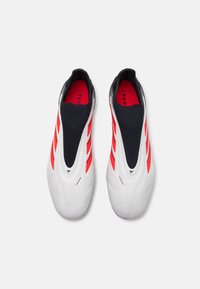 Bijele slip-on tenisice s crnim i crvenim naglasima, s elegantnim dizajnom i teksturiranim pletenim gornjištem. Značajne tri crvene pruge sa strane.