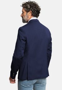 Blazer azul marino con tejido texturizado, solapas puntiagudas y detalles de puños con cuatro botones. Diseñado con un ventrículo central para facilitar el movimiento.