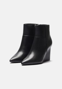 Bottines à talons compensés en cuir noir avec des bouts pointus, texture lisse, fermeture à glissière et silhouette moderne.