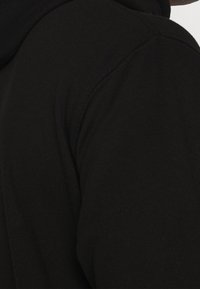 Felpa nera con una texture liscia, caratterizzata da un colletto alto e cuciture rinforzate lungo la cucitura della spalla. Design semplice e minimale.