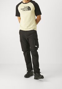 Sort og creme T-shirt med logo og korte ærmer, parret med sorte cargo bukser med sidelommer og sorte vandresko.