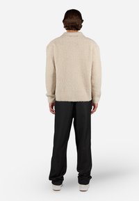 Cremefarvet, fluffy tekstur sweater med en foldet krave, drop-shoulder ærmer og ribbede manchetter, parret med løstsiddende sorte bukser og hvide sko.
