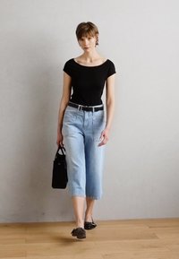 Svart tettsittende topp, lyseblå croppede jeans, svart belte, svart veske og svarte flate sko. Enkelt design med minimale detaljer.