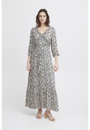 Maxi dress in cream with navy floral pattern, V-neck, three-quarter sleeves, cinched waist, and ruffled hem. Paired with beige block-heeled sandals.