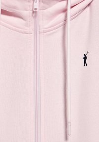 Felpa zipata rosa chiaro realizzata in tessuto morbido. Presenta un piccolo logo blu di un golfista sul lato sinistro del petto. Include cappuccio con lacci e tasche.