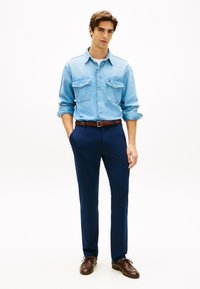 Ανοιχτό μπλε τζιν πουκάμισο με δύο τσέπες στο στήθος, σε συνδυασμό με σκούρο μπλε παντελόνι και καφέ δερμάτινα παπούτσια, με καφέ ζώνη.