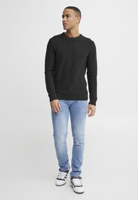 Zwart gebreid crewneck sweater, lichtblauwe distressed jeans en zwart-witte sneakers. Eenvoudig ontwerp met geribde manchetten.