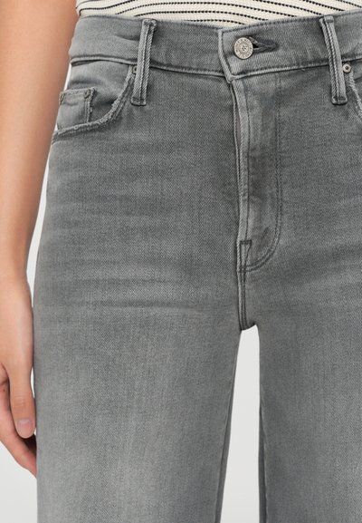 Close-up of a person wearing faded grey denim jeans with a buttoned waistband and pockets, alongside a striped shirt tucked in.