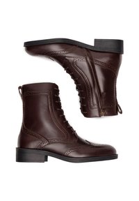 Pruunid nahast saapad, millel on ees paelad ja küljetõmblukk. Omavad brogue-detailidega mustrit ja madalat virnastatud kontsa. Sile tekstuur, hästi vormitud kuju.