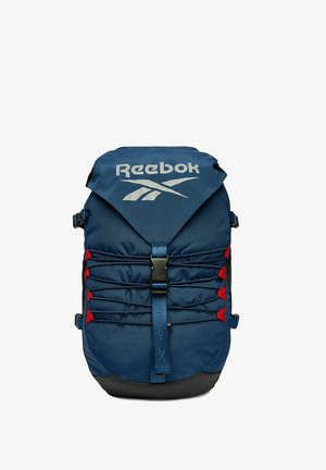 Blue Reebok backpack with top flap, black buckle, red accents, elastic cords across front, and Reebok logo in white on flap.