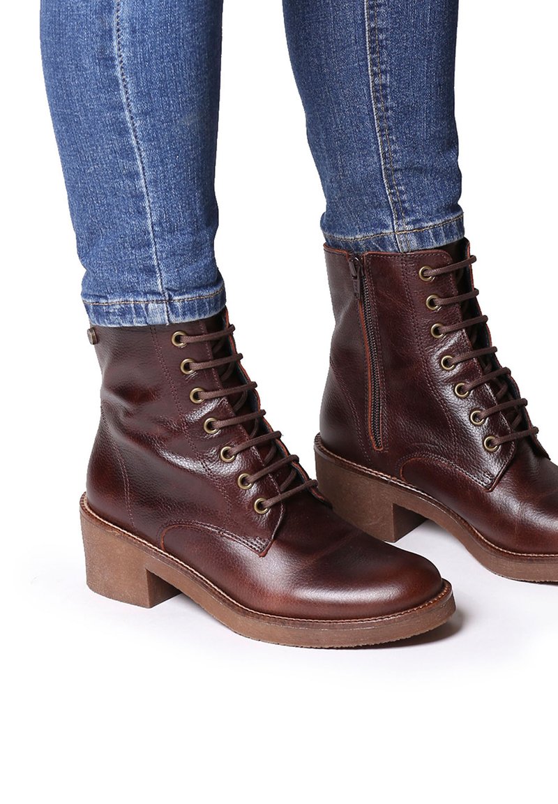 Botas de tobillo de cuero marrón con punta redonda, diseño de cordones y cremallera lateral. Suela gruesa y texturizada y ojetes de metal para los cordones.