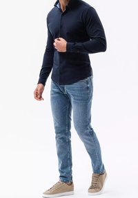 Marinblå långärmad knapp-up skjorta, figursydd design; ljus tvätt denim jeans; beiga sneakers med minimala detaljer; mjuka tyger; avslappnad stil.