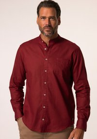 Camisa burdeos de manga larga con cuello alzado, bolsillo frontal y cierre de botones. Hecha de una tela texturizada, con botones a juego.