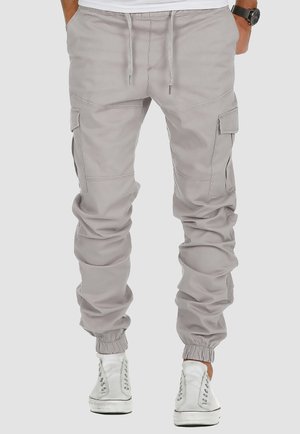 Mand iført lysegrå cargo joggerbukser med snøre i taljen og elastiske manchetter, kombineret med hvide high-top sneakers.