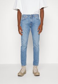 Light blue denim jeans with a slim fit, five-pocket design, and subtle whiskering, paired with beige lace-up boots and a white t-shirt.