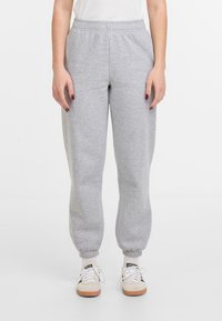 Pantalons de survêtement en jersey gris avec une taille élastique, des poignets côtelés et une coupe ample. Portés avec des baskets blanches et des chaussettes à motifs.