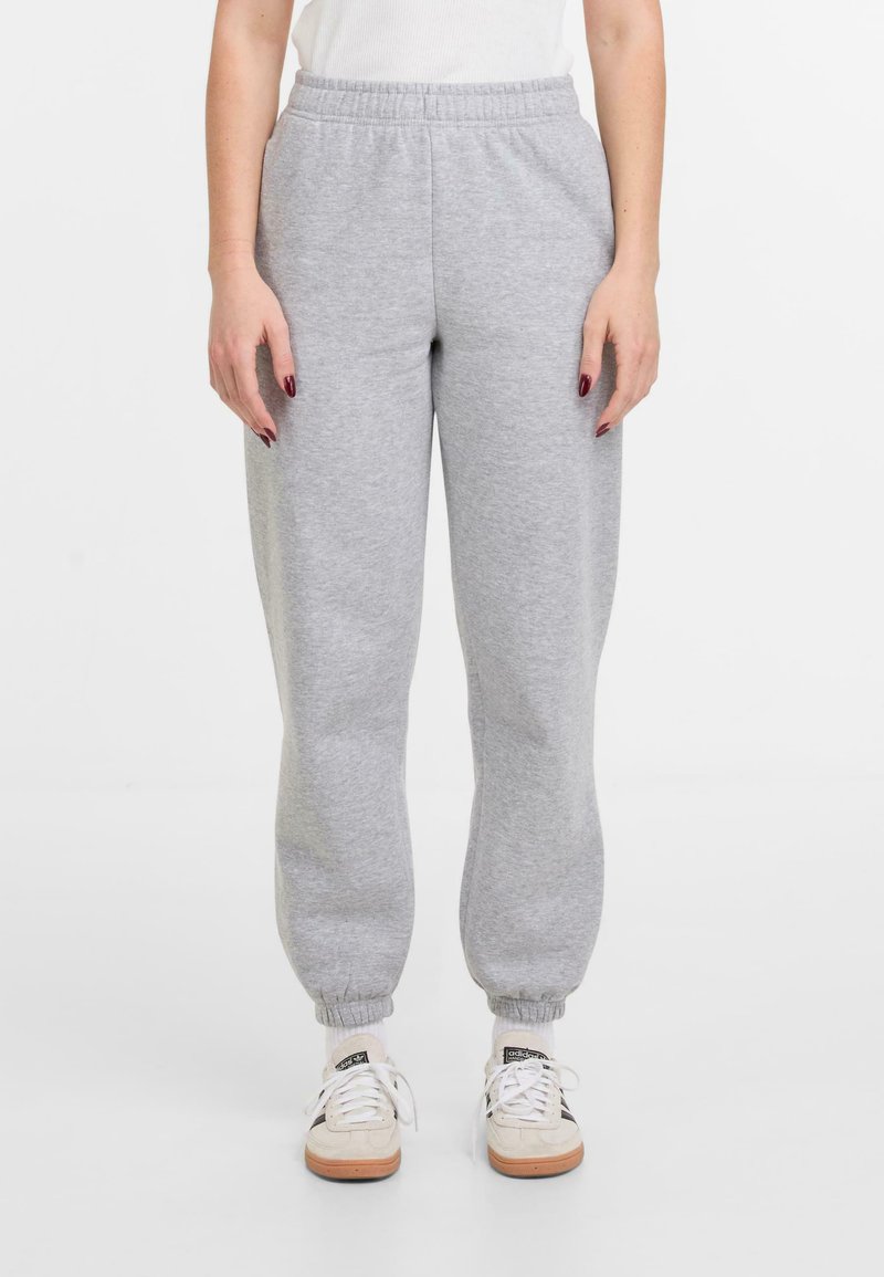 Pantalons de survêtement en jersey gris avec une taille élastique, des poignets côtelés et une coupe ample. Portés avec des baskets blanches et des chaussettes à motifs.
