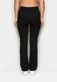 Czarne rozszerzane spodnie wykonane z elastycznego materiału, o gładkiej teksturze i elastycznym pasie, w zestawie z białymi sneakersami.