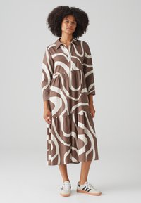 Brown and white patterned shirt dress with long sleeves, a collared neckline, and a tiered skirt. Worn with white sneakers.