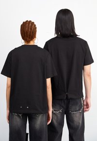 Camisetas de algodón negras, de corte relajado con mangas cortas. Los detalles notables incluyen un cierre en la parte posterior con broches y un acabado texturizado. Combinadas con jeans desgastados.