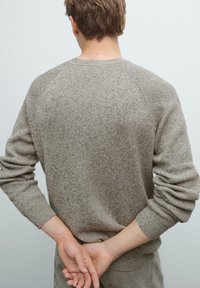 Lichtbruine gebreide trui met een gestructureerde afwerking, raglanmouwen en geribbelde manchetten. De stof lijkt zacht en comfortabel.