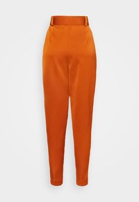 Oranje broek met een gladde textuur, lichaamsnauwkeurige pasvorm en een bijpassende riem in de taille. Voorzien van plooien voor extra detail en structuur.