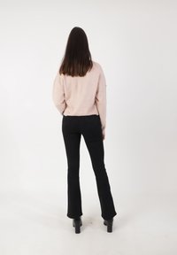 Jasnoróżowy sweter z dzianiny zestawiony z czarnymi dżinsami w dzwony i ciężkimi czarnymi obcasami. Sweter ma prążkowany dół i długie rękawy.