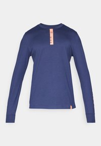 Tummansininen pitkähiha Nike-paita, jossa on vaaleanpunainen pystysuora logo rintamalla ja vaaleanpunaisia yksityiskohtia vasemmassa hihassa ja alareunassa.