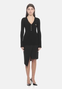 Schwarzer, gerippter Strickpullover mit V-Ausschnitt und langen Ärmeln, ausgestattet mit goldfarbenen Knöpfen und einer kleinen Brusttasche, kombiniert mit einem schwarzen asymmetrischen Rock.