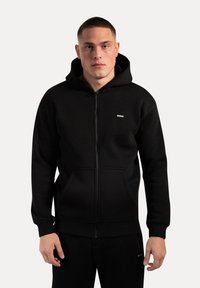 Sudadera con cremallera negra, con un bolsillo frontal, puños y dobladillo acanalados. Fabricada con material suave; presenta un pequeño logotipo en el pecho.