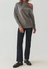 Grauer schulterfreier Pullover mit gerippten Bündchen und Saum, kombiniert mit dunkelblauen Schlagjeans und schwarzen Loafers mit dicken Sohlen.