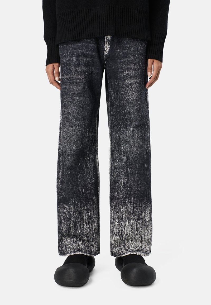 Schwarzer Pullover mit geripptem Saum, kombiniert mit weit geschnittenen Jeans, die einen verblassten Schwarz- und Gra gradients zeigen, getragen mit schwarzen Slippern.