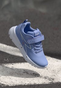 Chaussure de sport violet clair avec une tige en maille texturée, semelle en caoutchouc blanc, sangle Velcro et un design minimaliste avec des accents subtils.